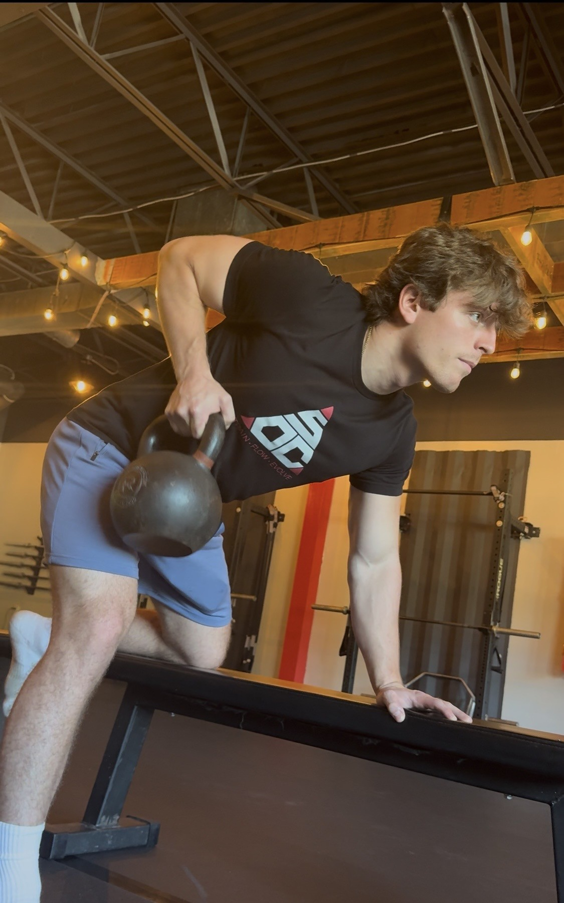 Mason Leavitt performing a single-arm kettlebell row on a bench in the studio.