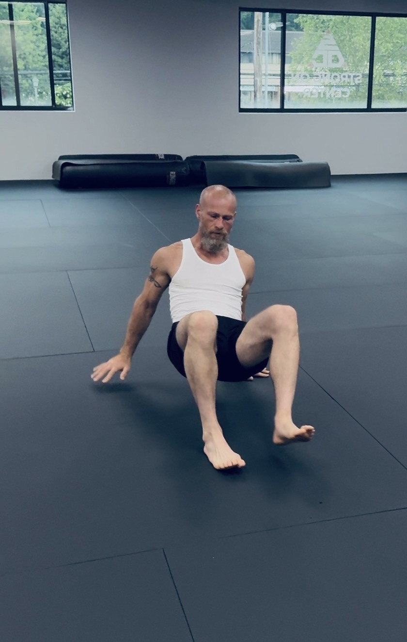 Coach performing a seated ground control mobility movement on the studio mat floor.